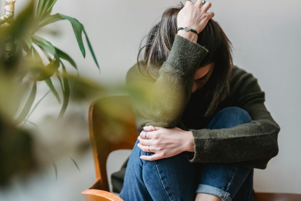 pexels-photo-6382642-6382642 Anonymous young sorrowed female in casual outfit touching dark hair and embracing knees while sitting on chair at home